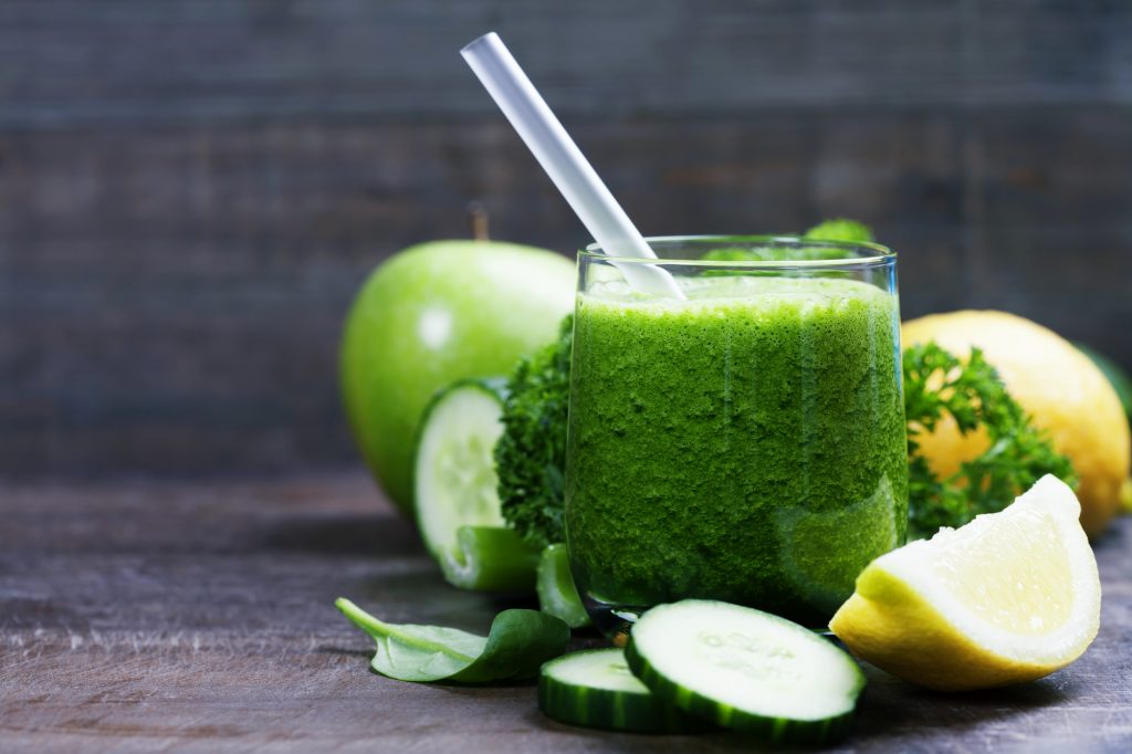 Fresh organic green smoothie with spinach, cucumber, parsley, celery and lemon on wooden background